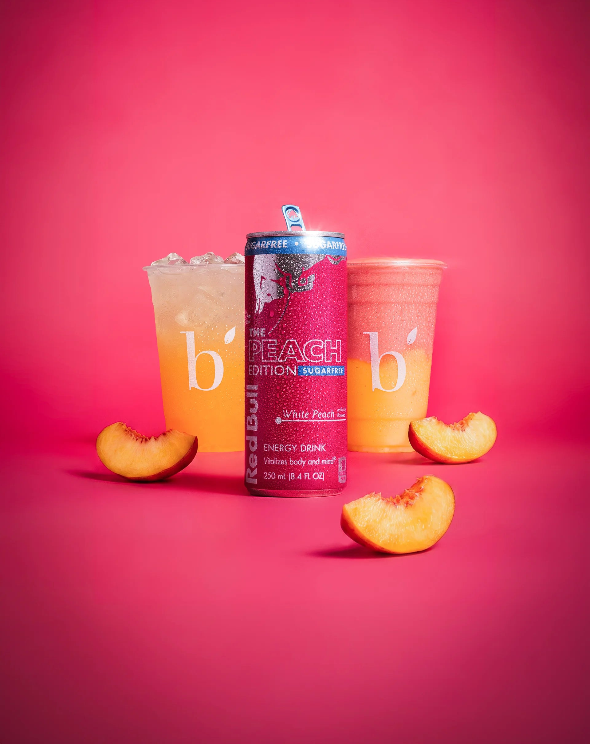 Red Bull Peach Edition drink centered in front of 2 beaming beverages with three peach slices on a pink background