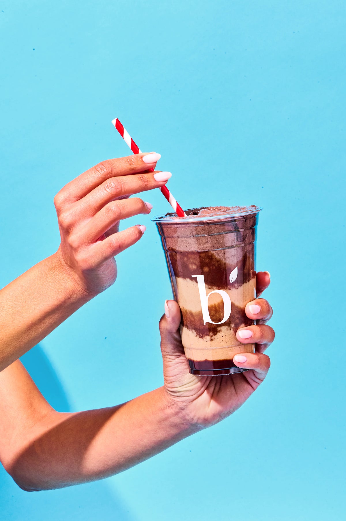 Hand holding a clear cup with a layered drink and a red straw against a blue background