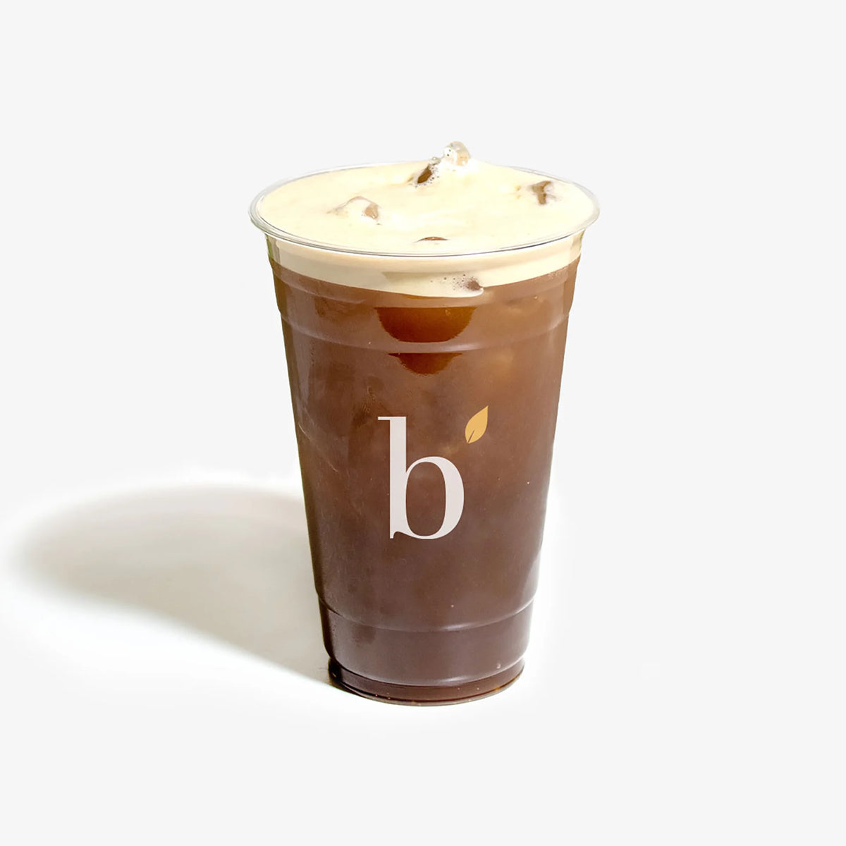 An iced coffee in a clear plastic cup with a white logo, topped with a thick layer of whipped cream, on a light gray background.