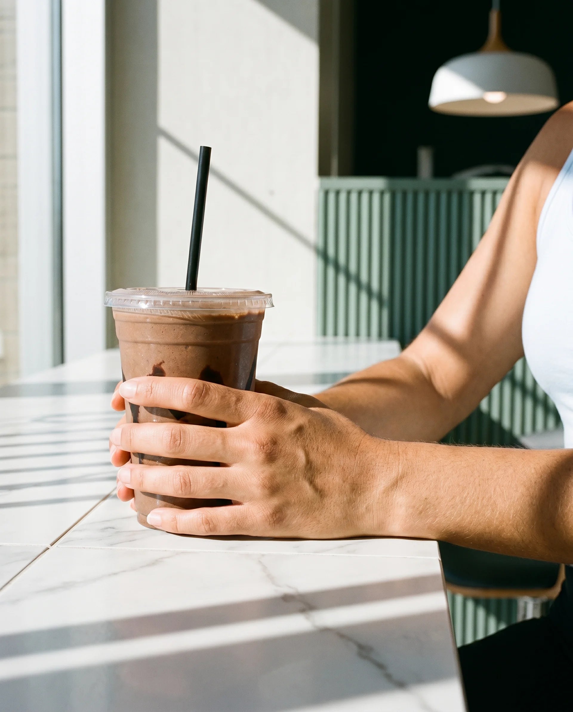 Person holding a iced coffee drink with a straw in an outdoor setting