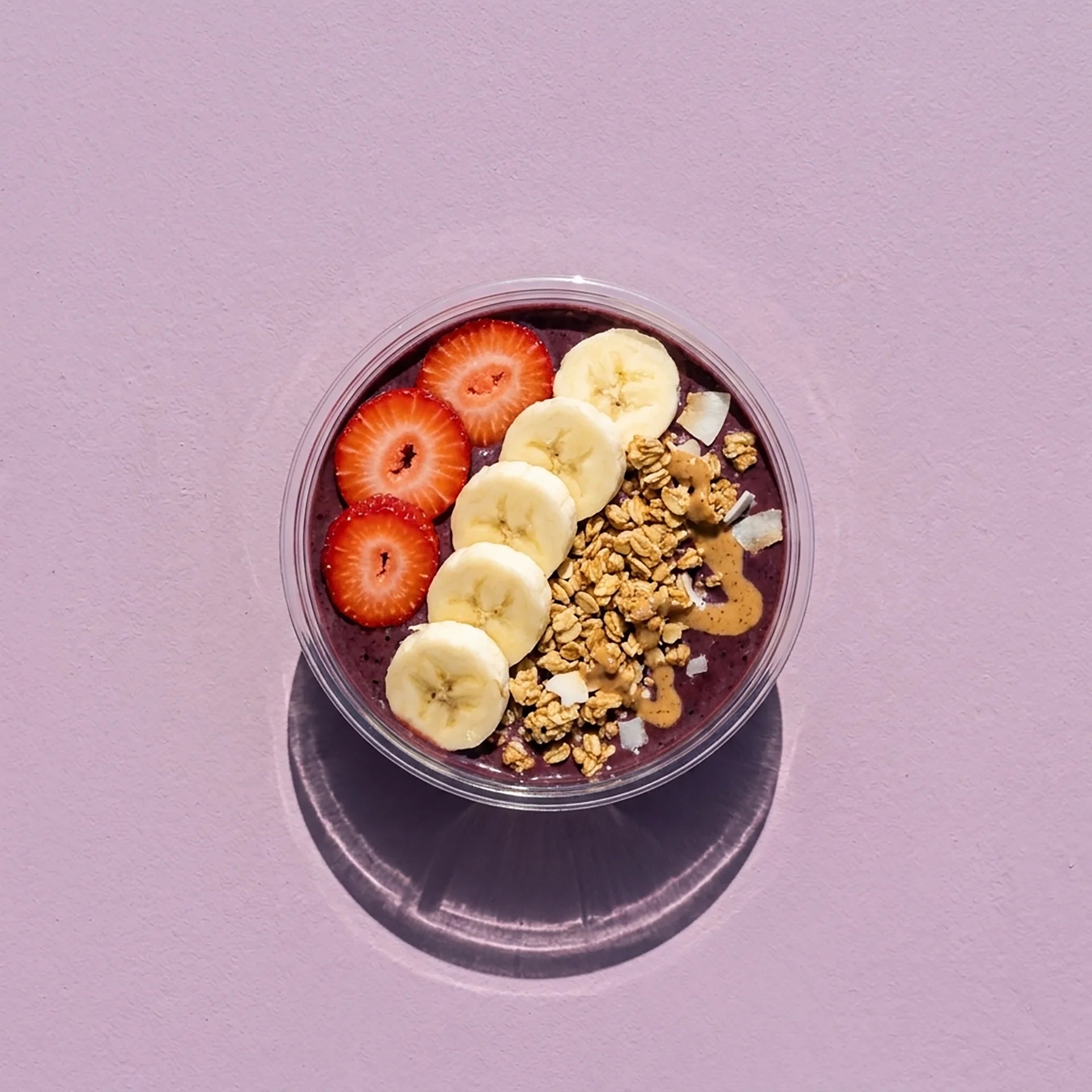 Acai bowl with strawberries, bananas, and granola on a purple background