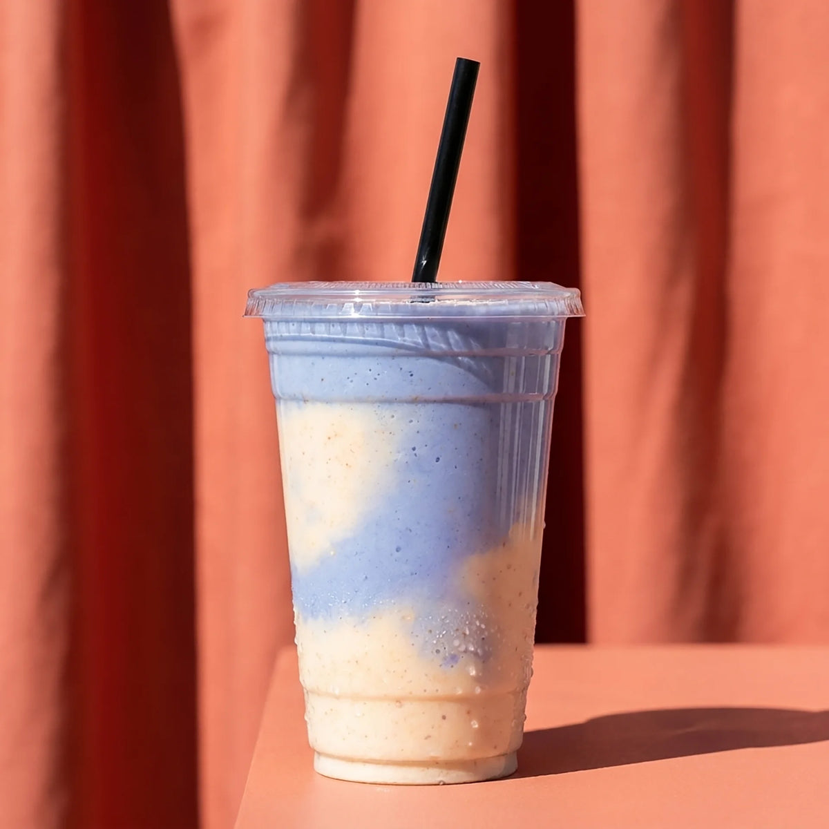 Clear plastic cup with a layered drink and black straw against a red background