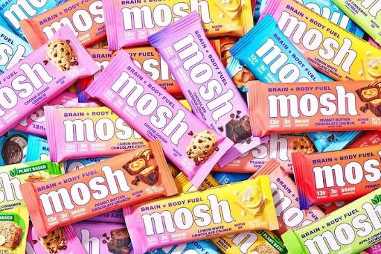 A close-up, top-down view of multiple Mosh branded protein bars in different flavors, including pink, orange, yellow, blue, and green wrappers, overlapping each other.